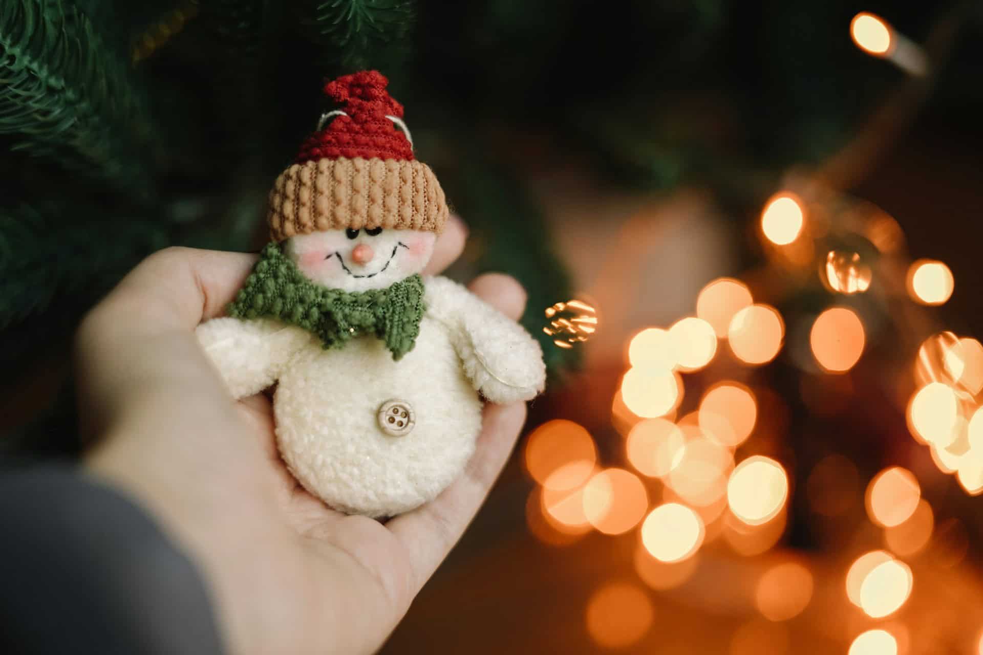 Hand holding a small knitted Christmas snowman decoration with festive lights in the background