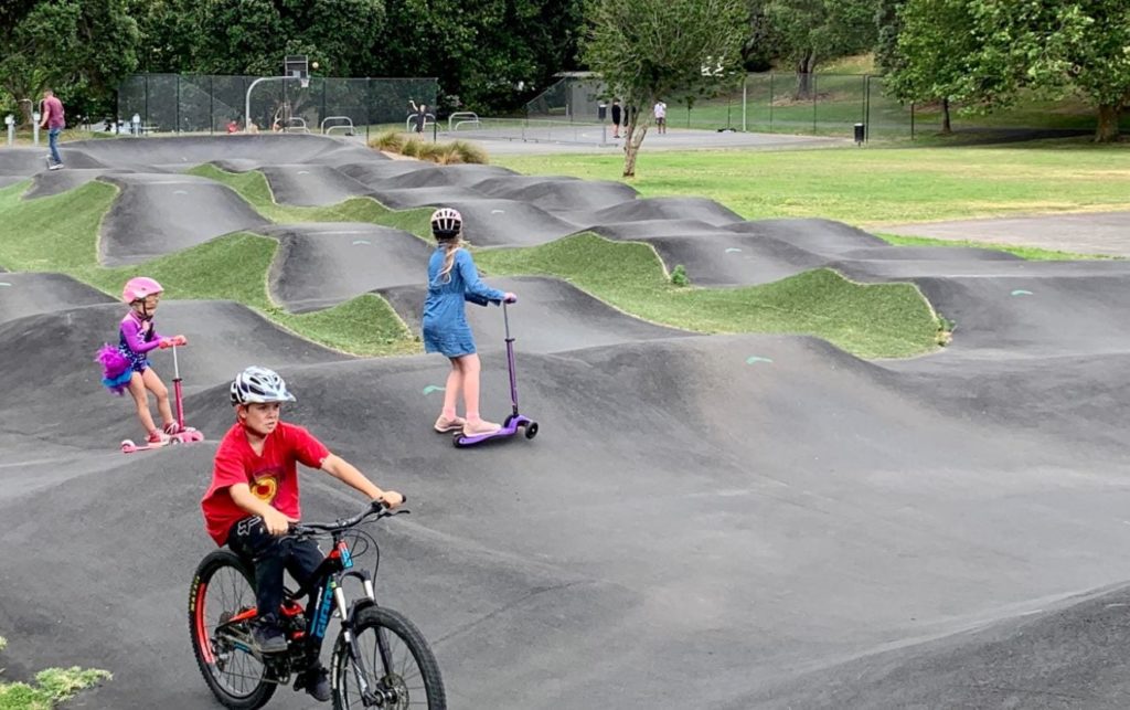 Children biking and riding scooters on the Pump Track at Grey Lynn Park | Auckland for Kids