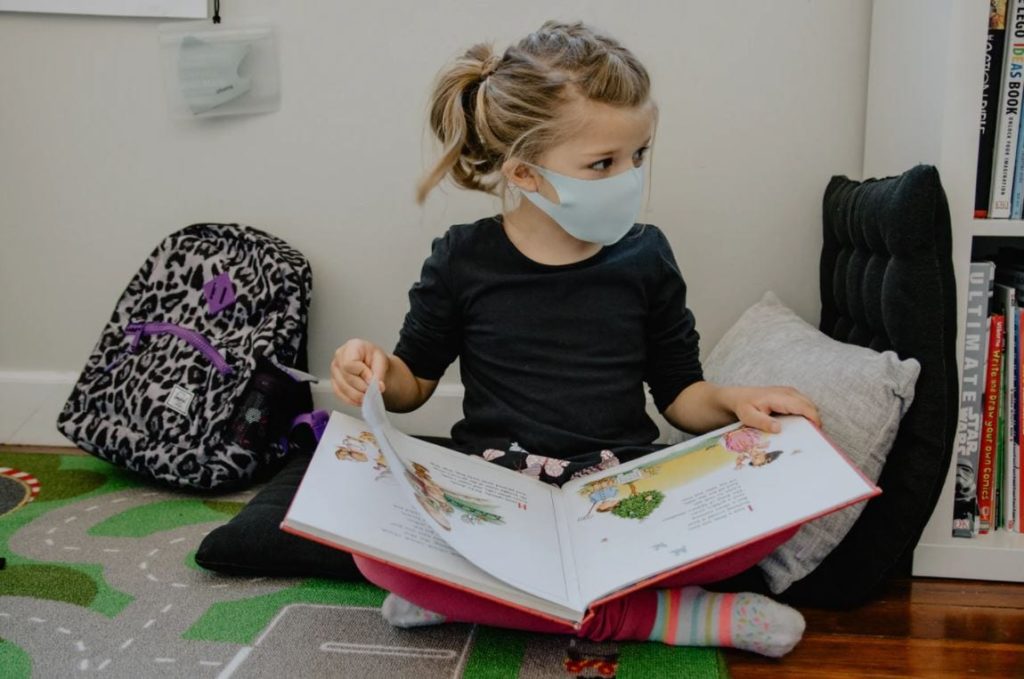 Child wearing a COVID mask reading a book