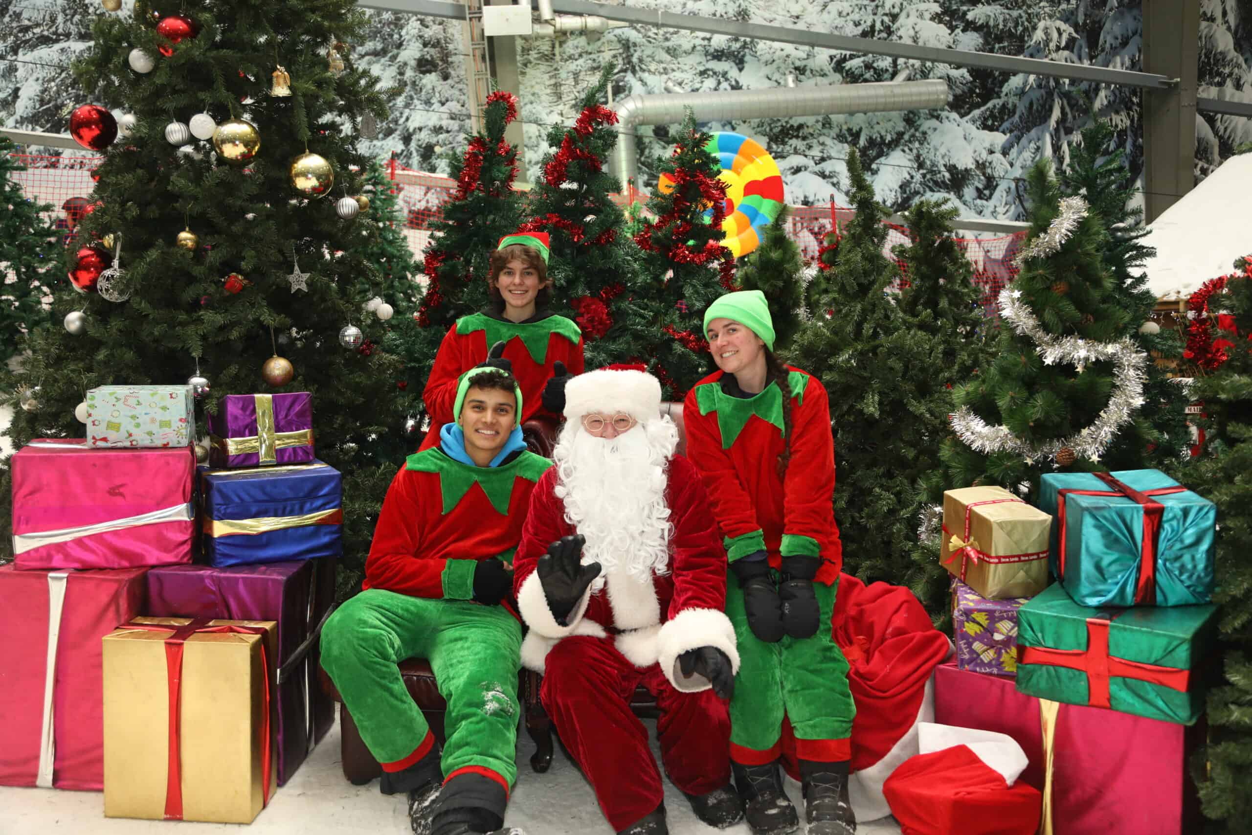 Santa with his elves sitting among Christmas trees and presents at Snowplanet