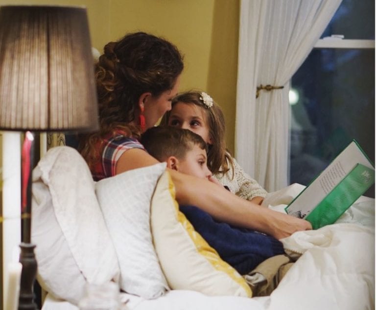 Family reading a book together in bed with Mum