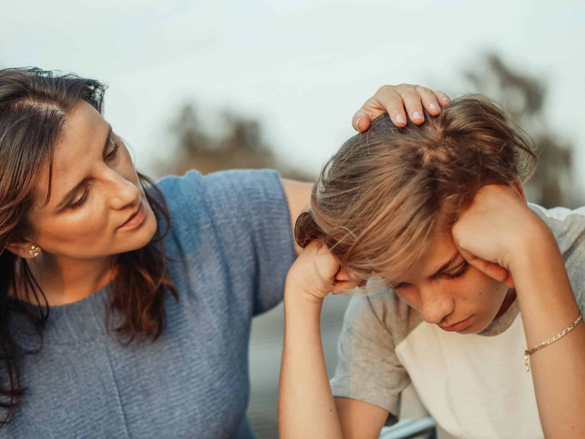 Woman gently comforting a sad boy with her hand on his head
