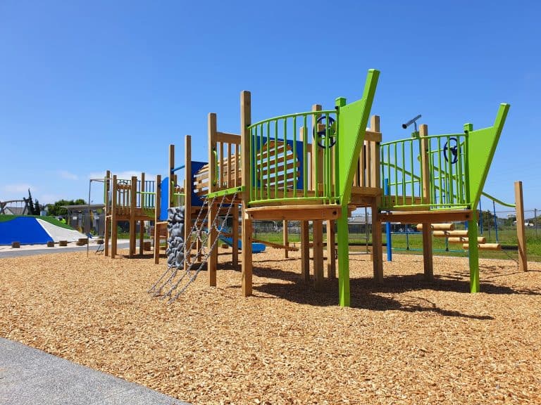 Playground climbing structure with slides, rope nets and steering wheels at Favona Playground in Māngere under a bright blue sky