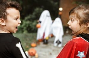 Children in Halloween costumes laughing and reacting to kids dressed as ghosts.