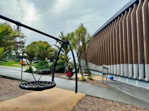 Small modern playground outside Birkenhead Library with a basket swing, ride-on toys and musical play elements.