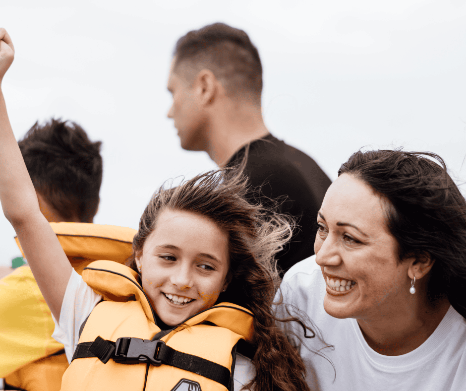 Smiling family sailing on a boat with children wearing lifejackets and wind blowing through their hair