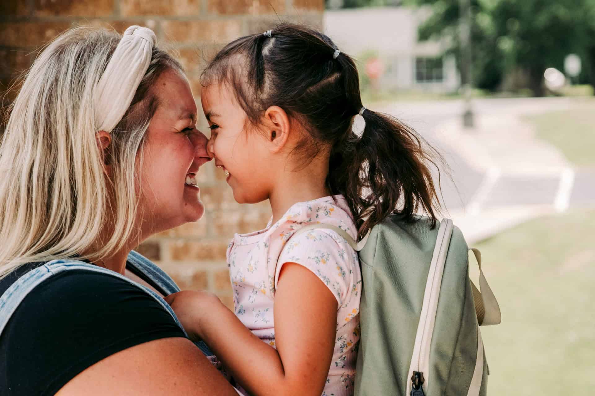 Mother and daughter smiling with their foreheads touching outside school
