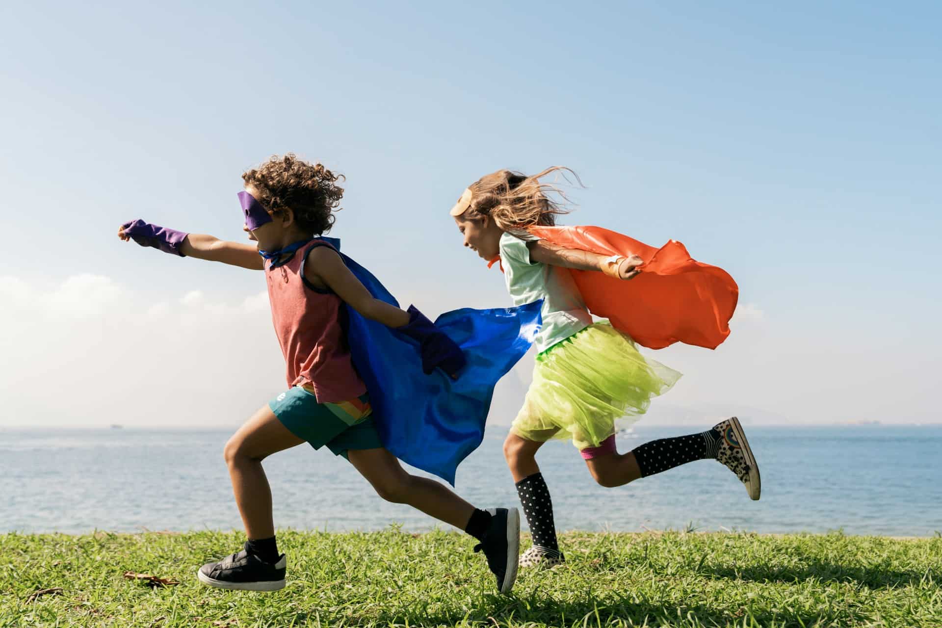 Two young children dressed as superheroes running outside near the water