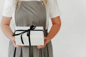 Person in apron holding a white gift box with a black ribbon