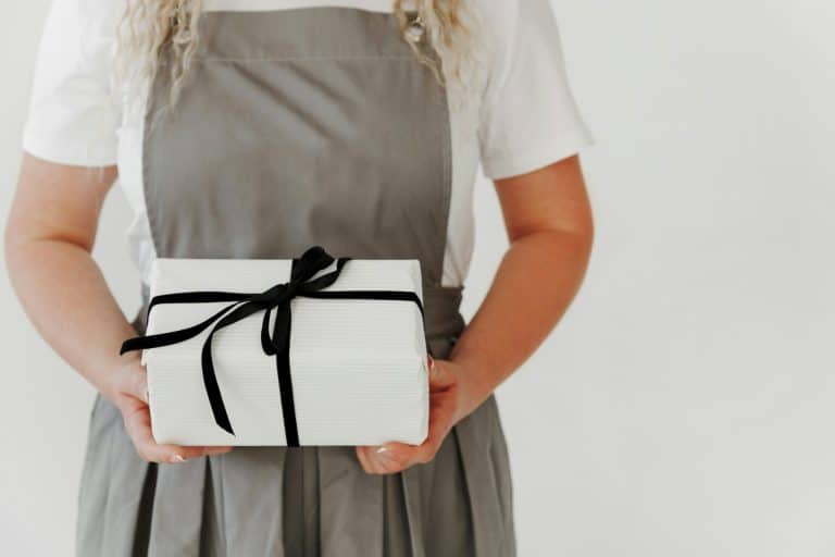 Person in apron holding a white gift box with a black ribbon