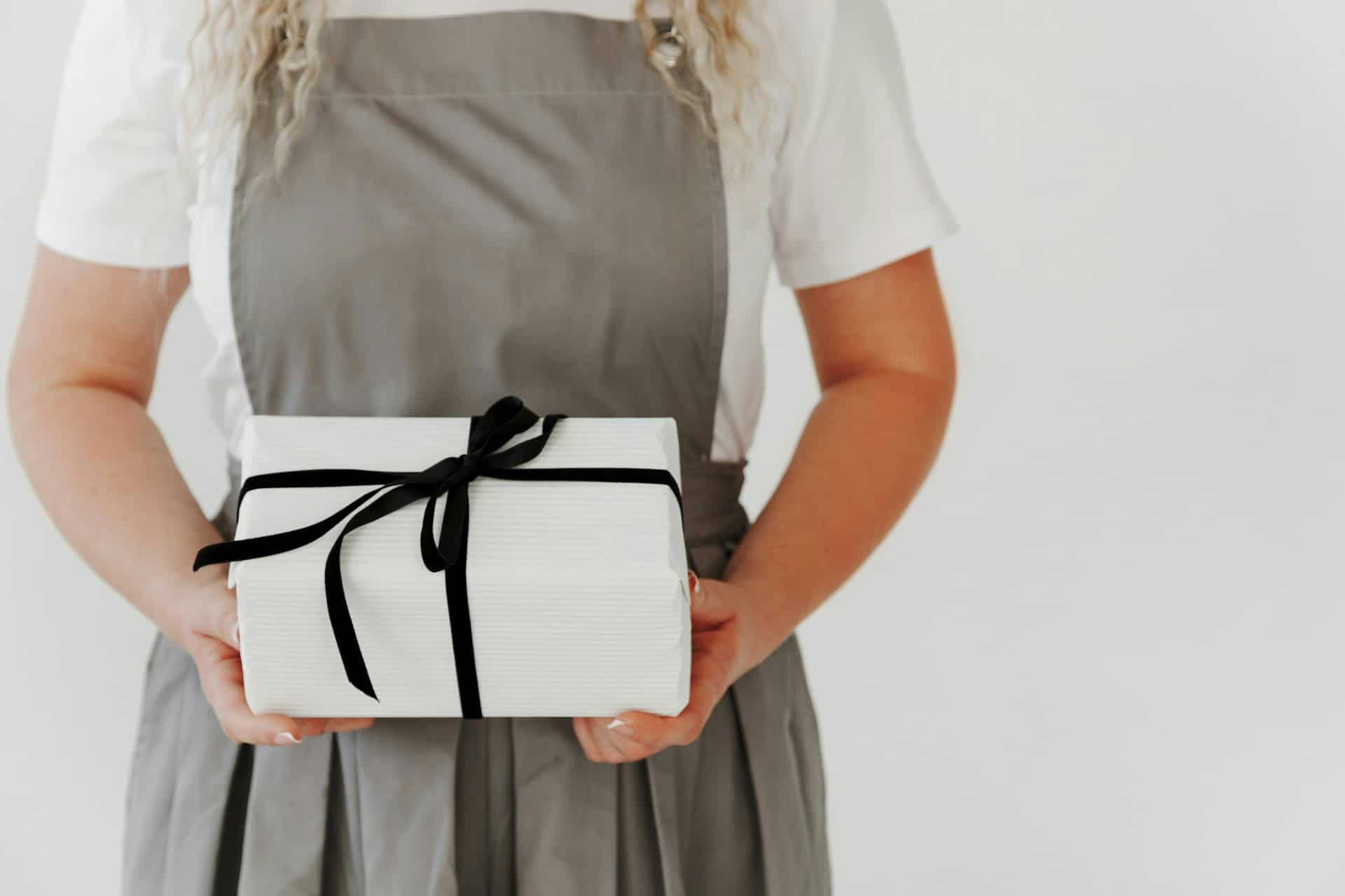 Person in apron holding a white gift box with a black ribbon