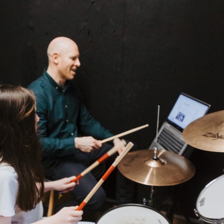 Child learning to play drums with an instructor at a modern music holiday programme