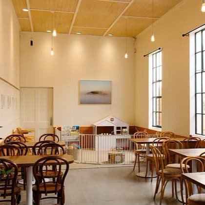 Family-friendly cafe interior at Stone Oven in Devonport, showing wooden tables and chairs, high ceilings and a small children's play area with books and toys