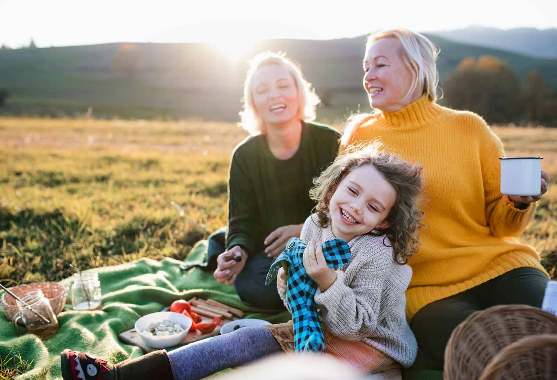 Smiling child with two women enjoying a sunny outdoor picnic