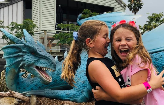 Two girls laughing in front of a blue dragon statue at Butterfly Creek in Auckland