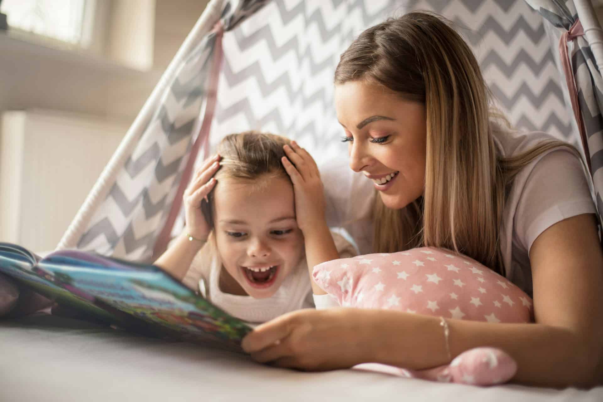 Mother and daughter reading a picture book together inside a play tent.