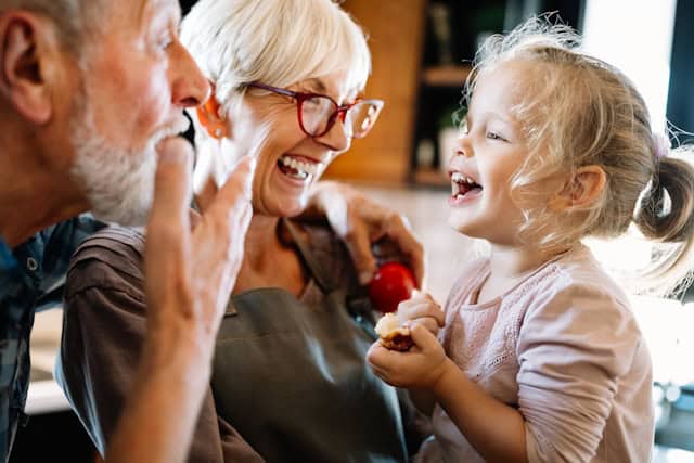 Grandparents laughing and spending time with their granddaughter in the kitchen.