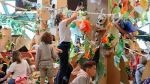 Children and families building a colourful forest installation using paper, tape and recycled materials at Paper Planet by Polyglot Theatre.