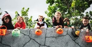 Children in Halloween costumes holding pumpkin buckets at an outdoor event.