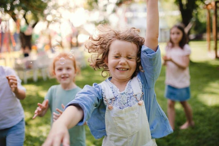 Smiling child playing with bubbles at a family event in a park