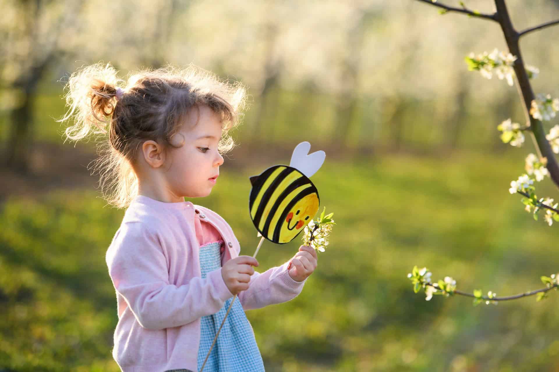 Child holding a bee cutout and looking at blossom on a sunny spring day
